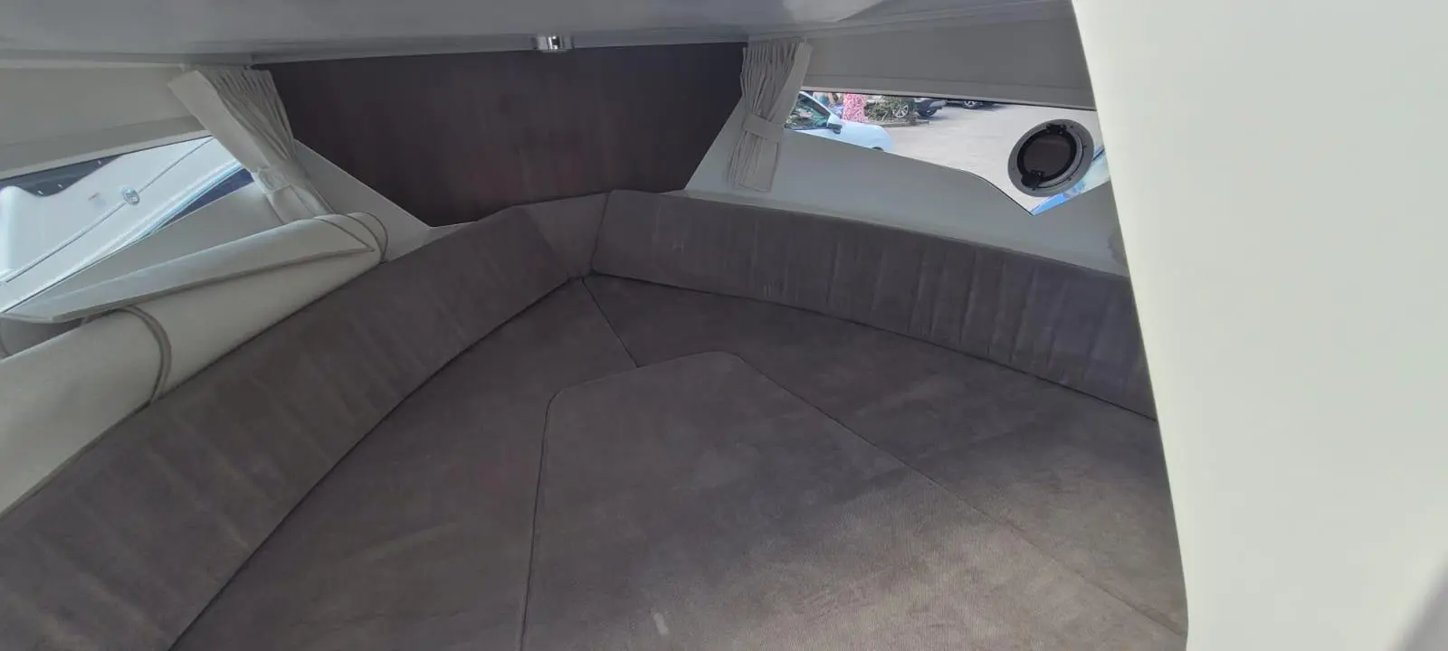 Interior view of a boat cabin featuring a large cushioned seating area with a window and decorative curtains.